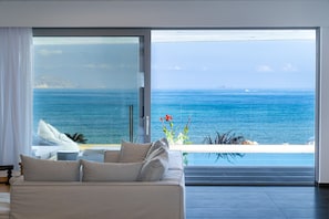 Una sala moderna con un gran ventanal que da a un balcón con vistas al océano.