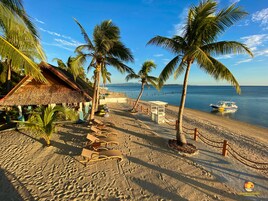 Un resort en la playa con cabañas de techo de paja, palmeras y un bote en el agua.