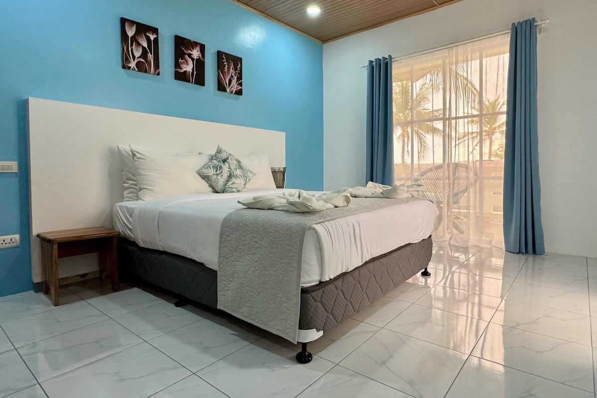 A bedroom with a bed, a nightstand, a window with curtains, and wall art.