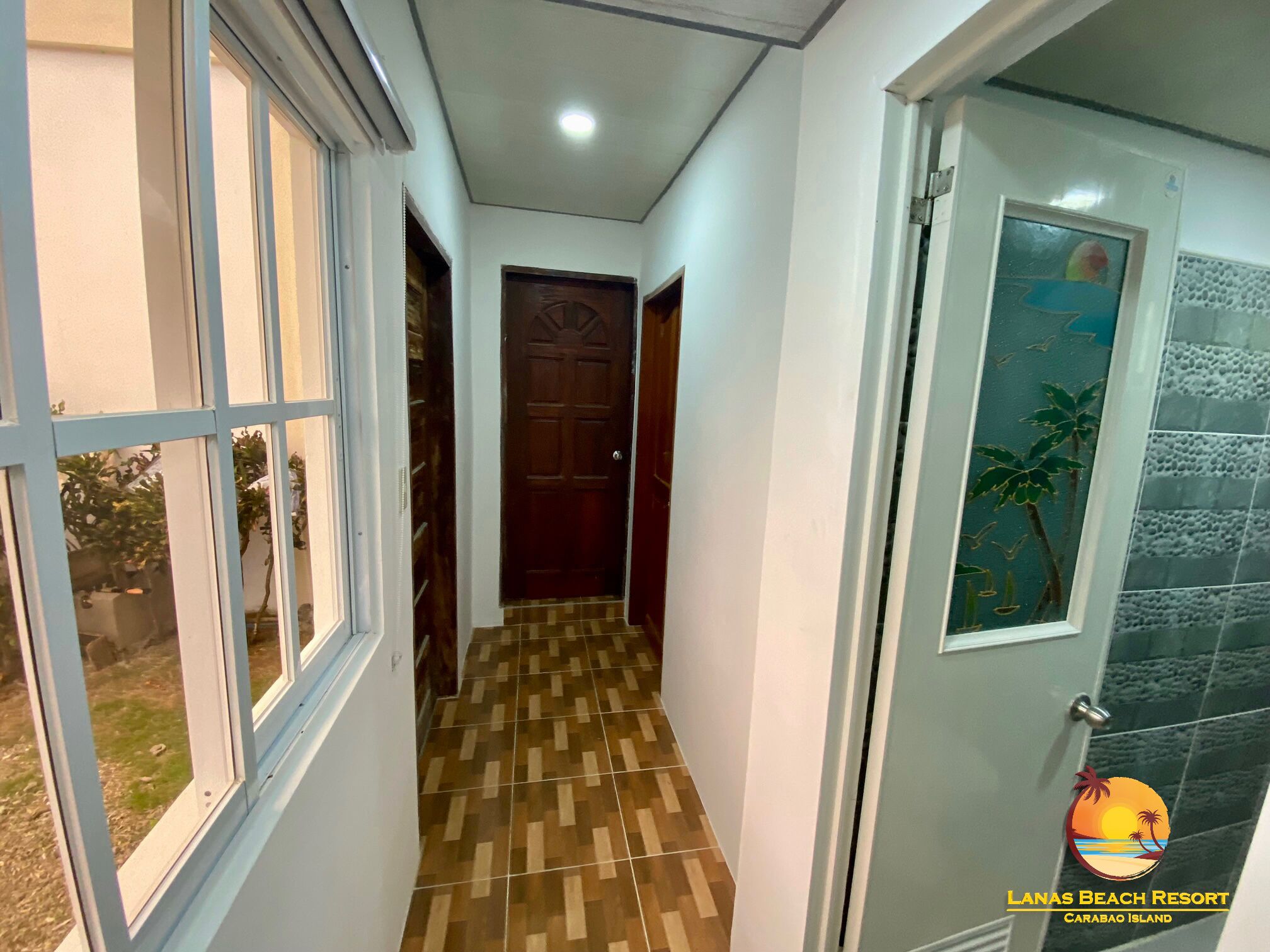 A hallway with patterned flooring, a wooden door, and a glass door with a tropical mural.