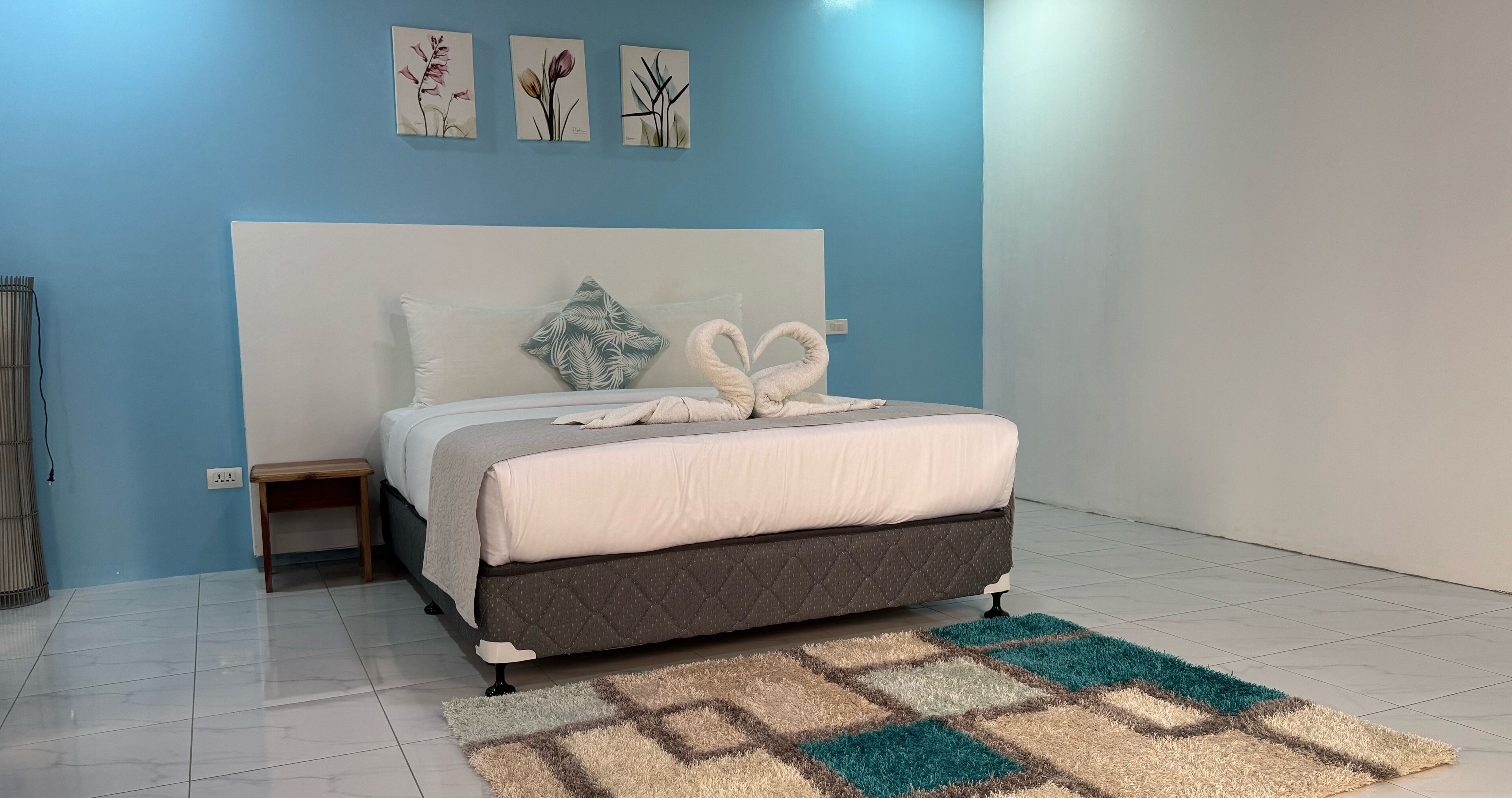 Une chambre à coucher comprenant un lit, une table de chevet, une prise électrique fixée au mur et un tapis à motifs.