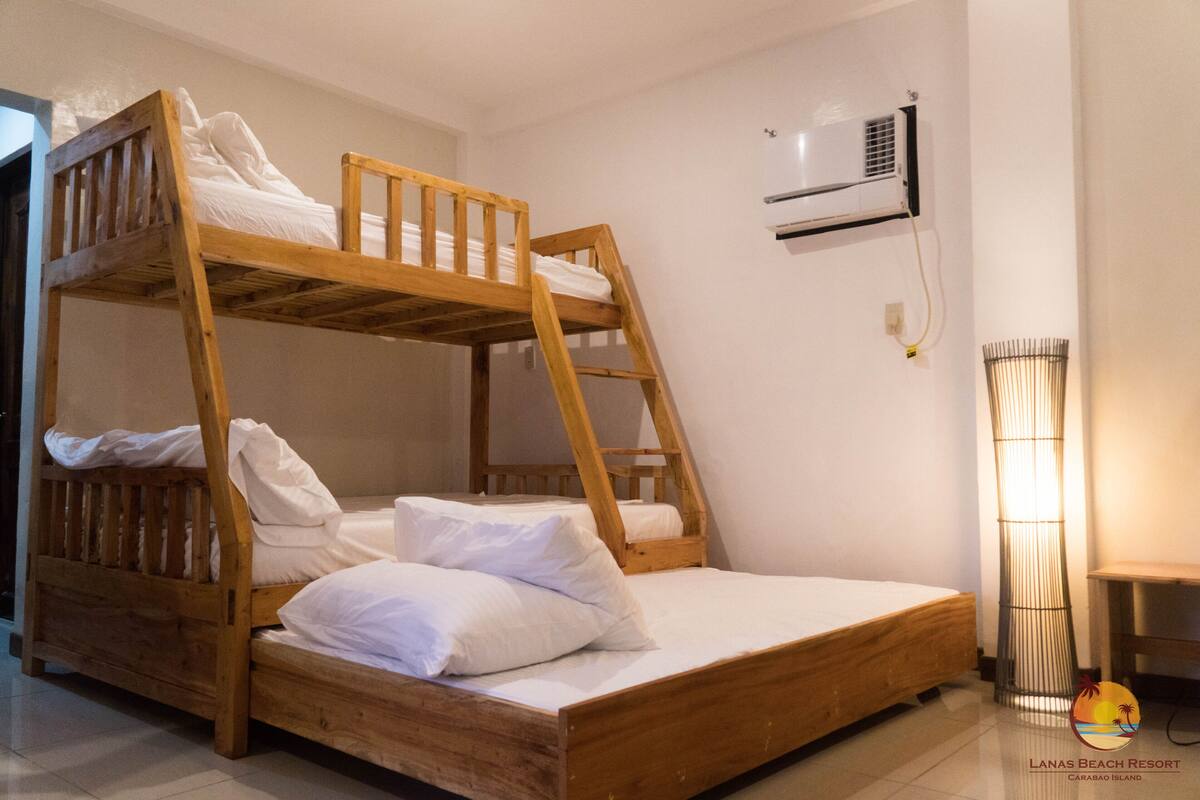 A bunk bed room with a wooden frame, white bedding, an air conditioning unit on the wall, and a floor lamp.