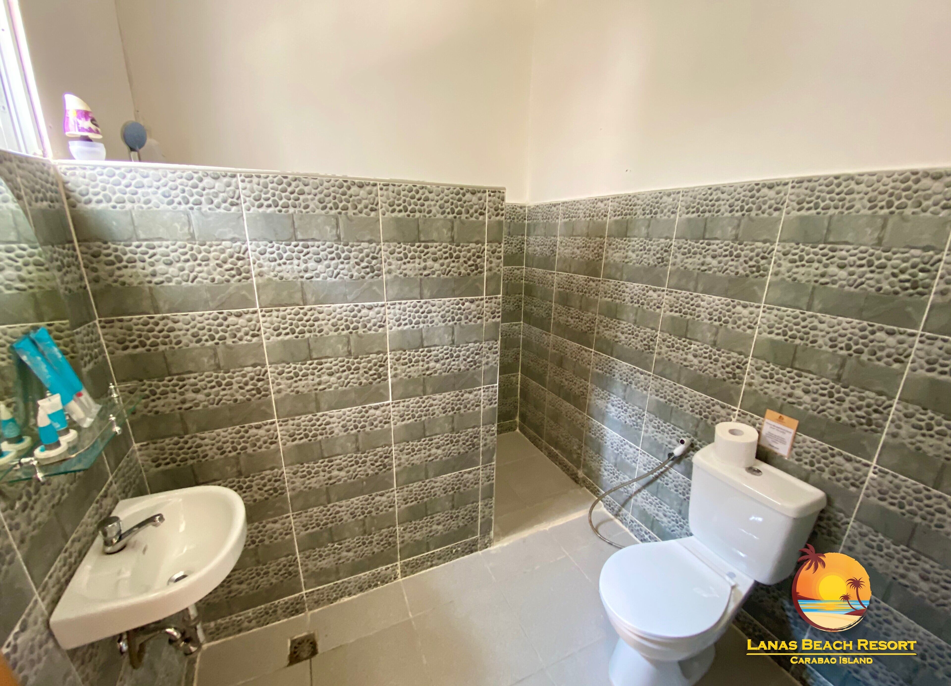 A bathroom with a sink, toilet, and shower area, featuring pebble-patterned tiles.
