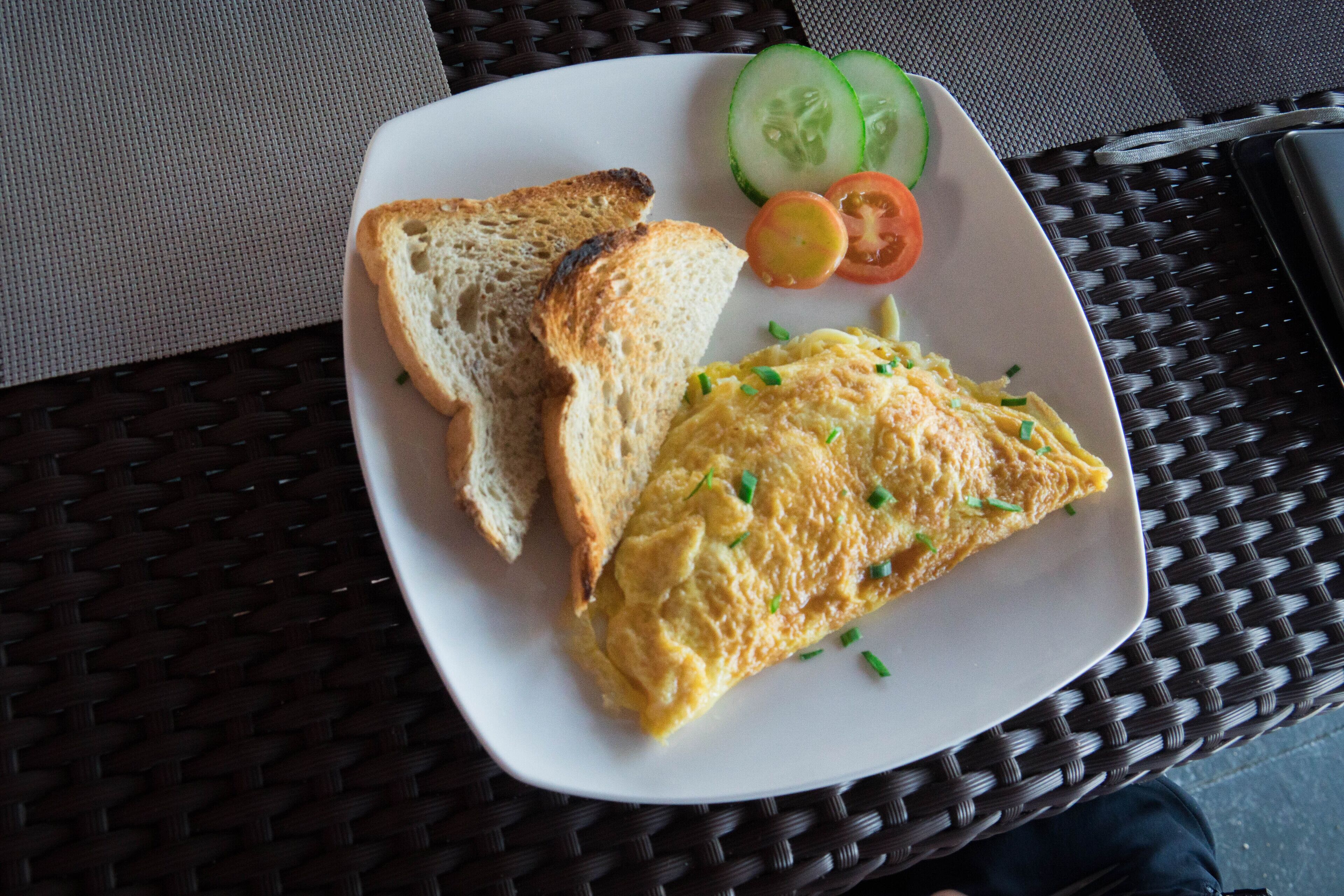 Un plato con tostadas, huevos revueltos, rodajas de pepino y medio tomate sobre una mesa tejida.