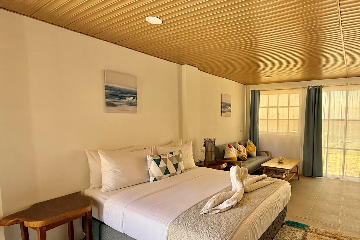 A hotel room with a large bed, a wooden ceiling, and a view of the outdoors through the window.
