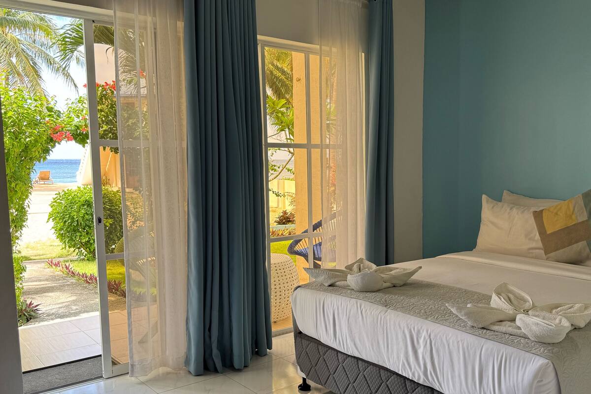 A hotel room with a bed, a view of the beach, and a sliding glass door.