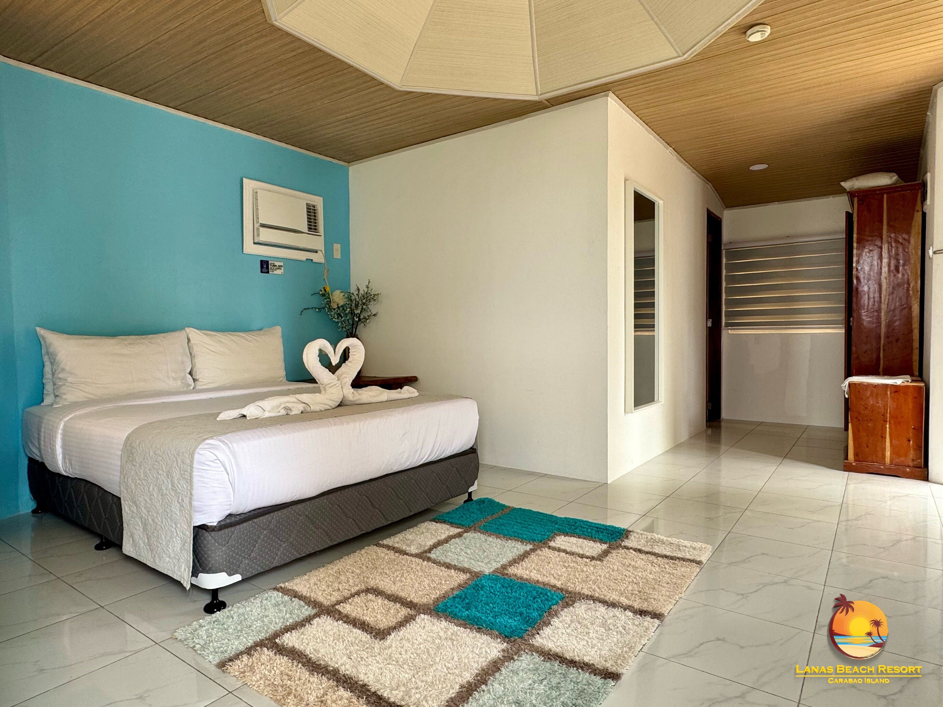 A modern bedroom with a bed, a heart-shaped towel arrangement, a small plant, and a checkered rug.