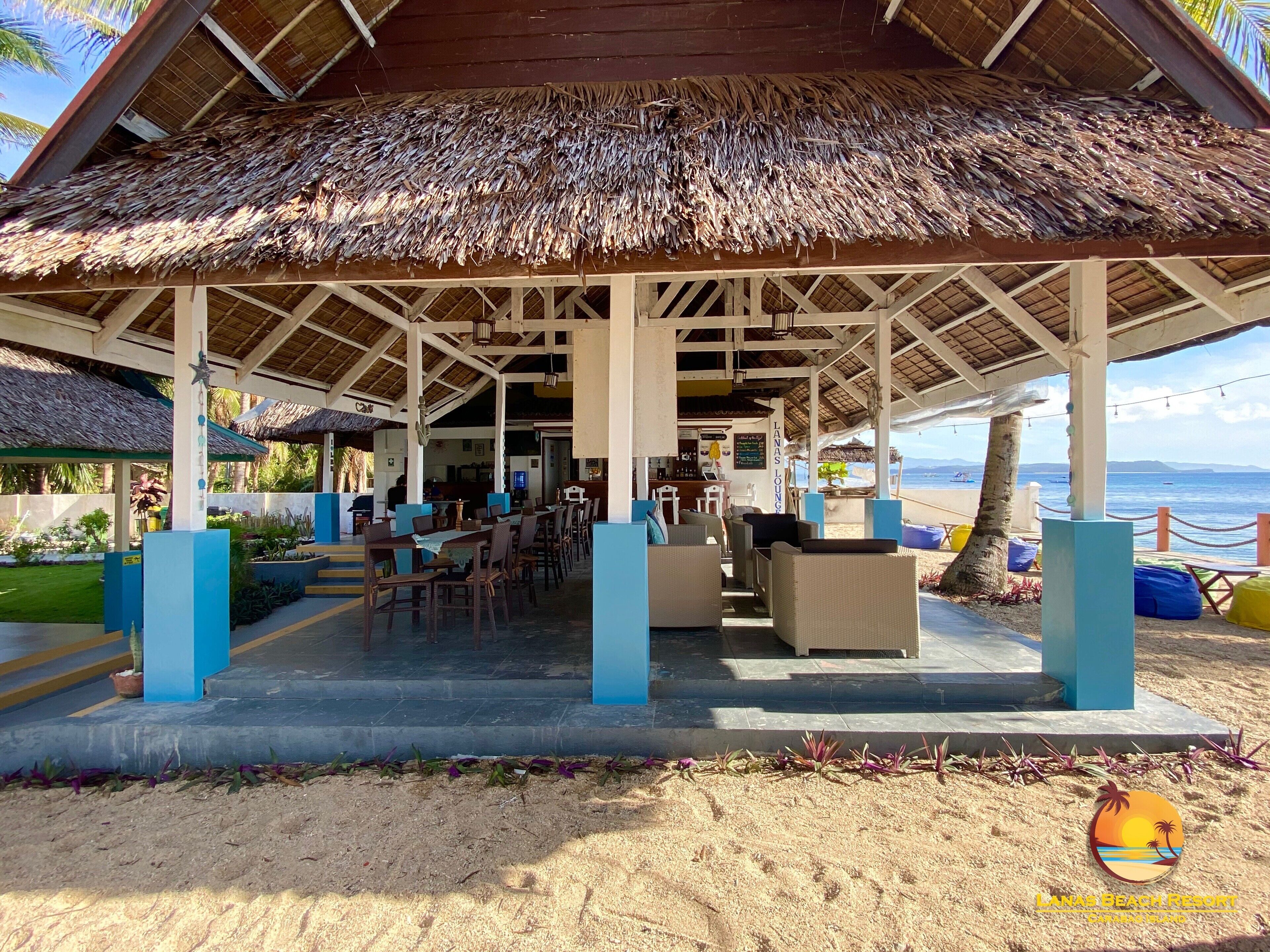 A beachside lounge with thatched roofs, outdoor seating, and a view of the ocean.