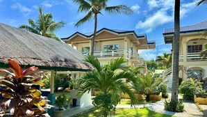 Un resort con varias edificaciones, una construcción de techo de paja y exuberante jardinería tropical.