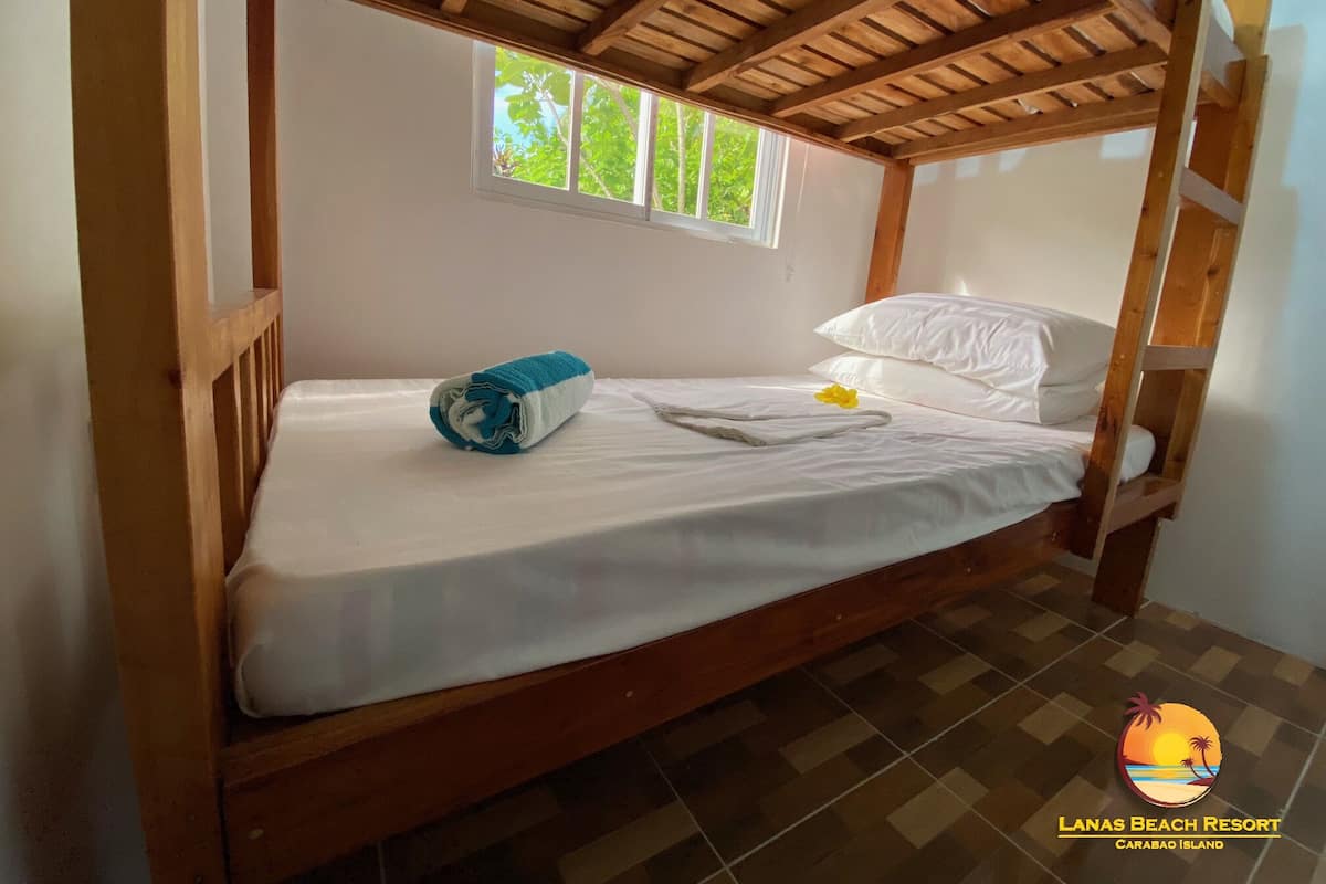 A single bed with a wooden frame, a window, and a view of greenery outside.