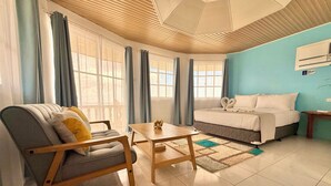 A modern hotel room with a bed, a sofa, a wooden table, and large windows with curtains. - Lanas Beach Resort - Carabao Island (Carabao Island)