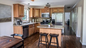 A modern kitchen with wooden cabinets, stainless steel appliances, and a bar area with stools. - Modern, Sauna, Near Whiteface/Lake Placid, Dogs, Mountain Views (Wilmington)