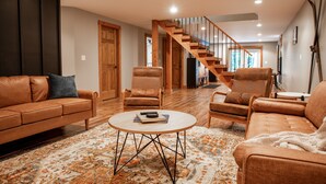 A spacious living room with a wooden staircase, leather sofas, and a round coffee table. - Modern, Sauna, Near Whiteface/Lake Placid, Dogs, Mountain Views (Wilmington)