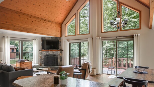 A spacious living area with a stone fireplace, large windows, and a wooden ceiling. - Modern, Sauna, Near Whiteface/Lake Placid, Dogs, Mountain Views (Wilmington)