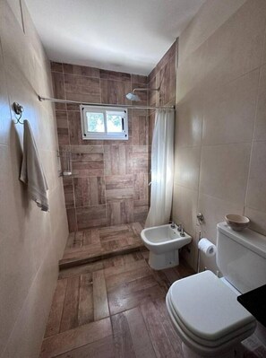 Bathroom features a shower area with a glass door and a window above, a toilet with a separate tank, and a towel hanging on the wall.