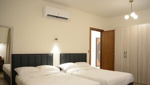 A hotel room with two beds, a wardrobe, an air conditioning unit, and a bedside lamp. - White Palace Motel EG (New Cairo)