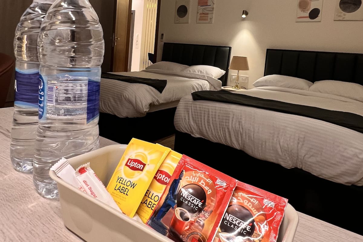 Habitación de hotel con dos camas, una mesita de noche, una botella de agua y una bandeja con bolsitas de té Lipton.