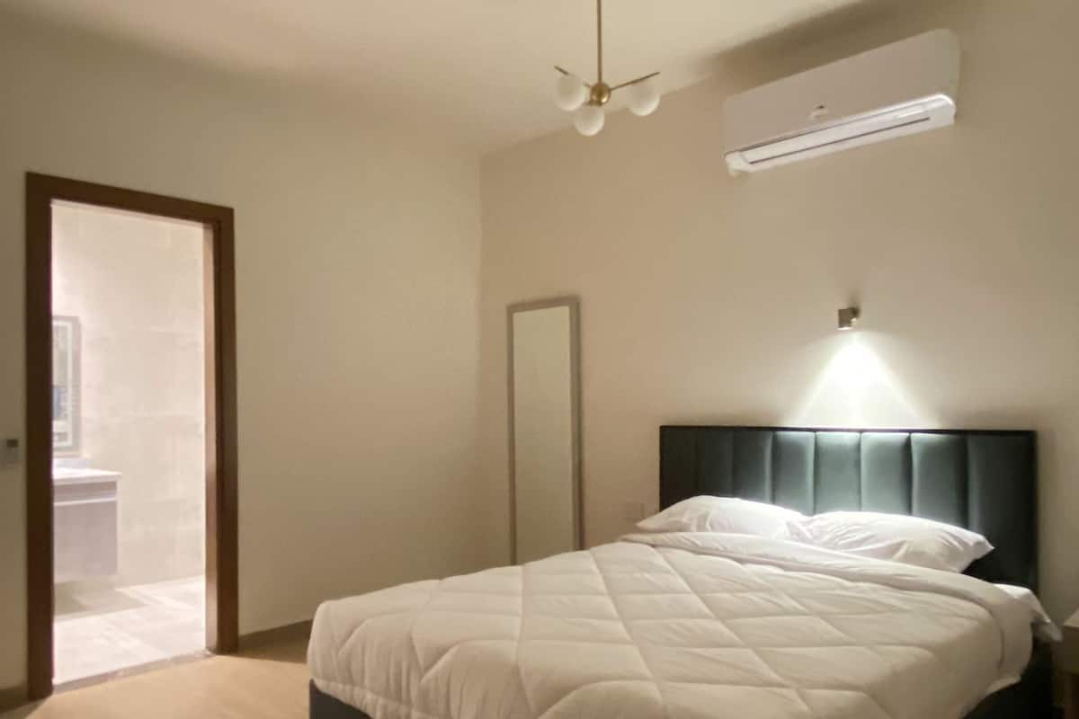 Un dormitorio con cama, ventilador de techo, espejo y aire acondicionado instalado en la pared.