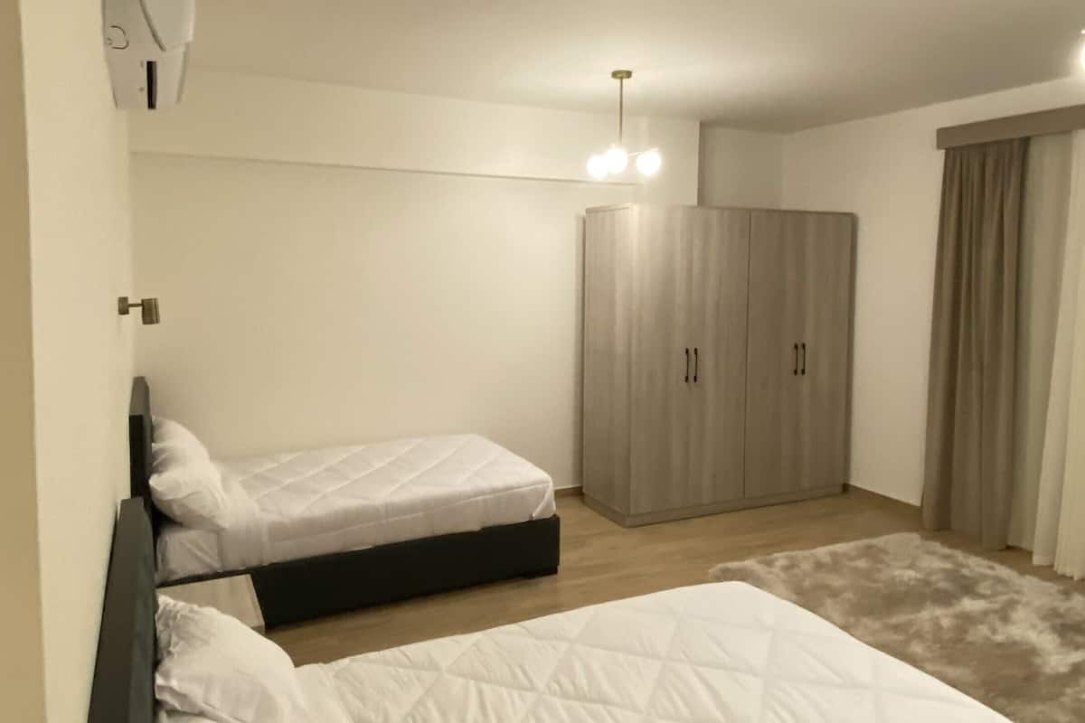 Un dormitorio con dos camas, un armario, una lámpara en el techo y una ventana con cortinas.
