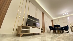 A modern living room with a flat-screen TV on a wooden stand, a dining area with dark chairs, and a marble floor. - White Palace Motel EG (New Cairo)