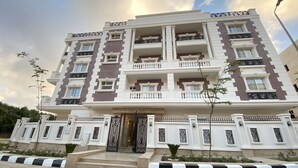 A multi-story building with a symmetrical facade, featuring a central entrance with a decorative gate, balconies with ornate railings, and a consistent brick pattern. - White Palace Motel EG (New Cairo)