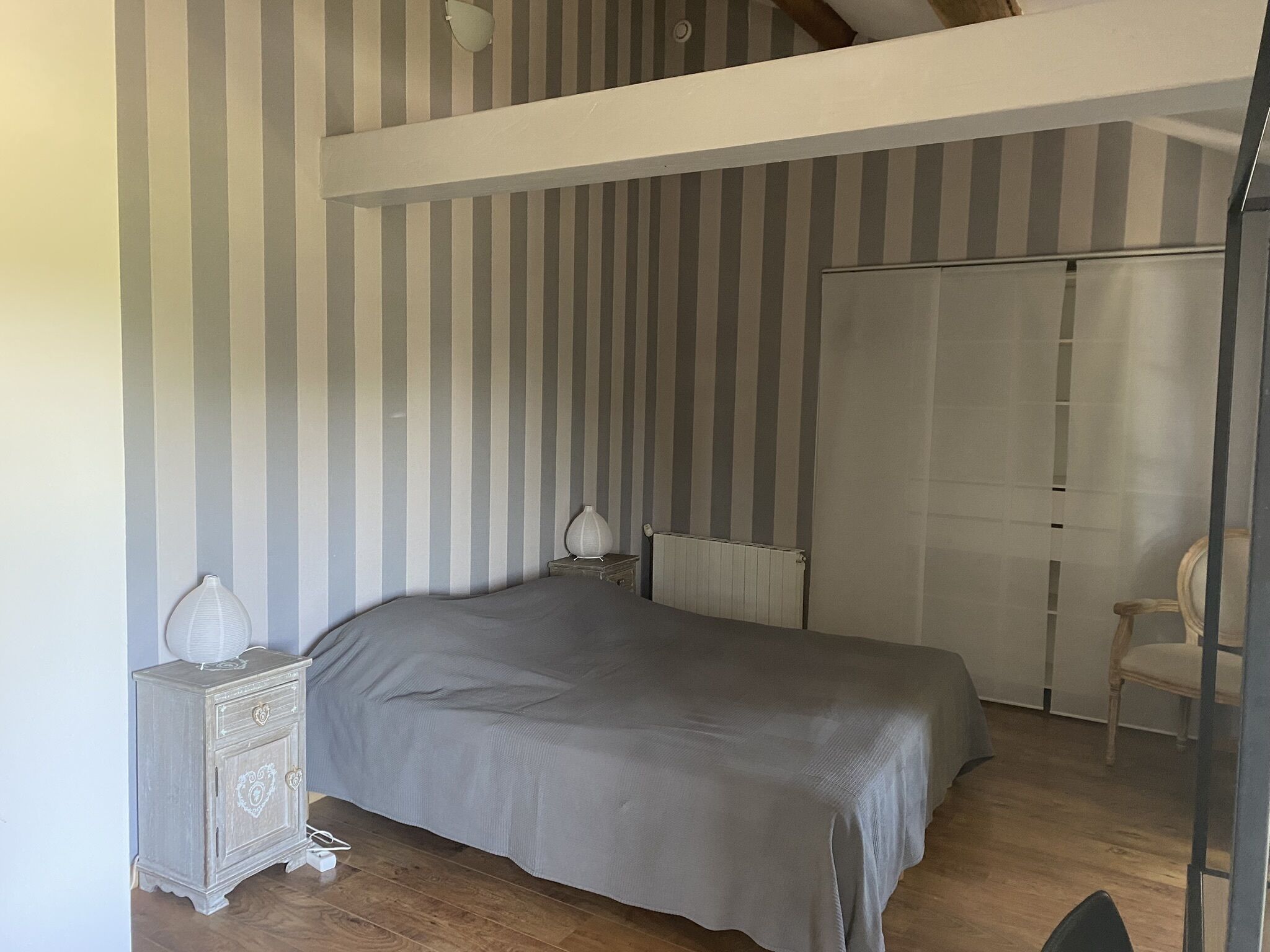 Une chambre à coucher comprenant un lit, une table de chevet, une commode, un radiateur et un placard avec porte coulissante.