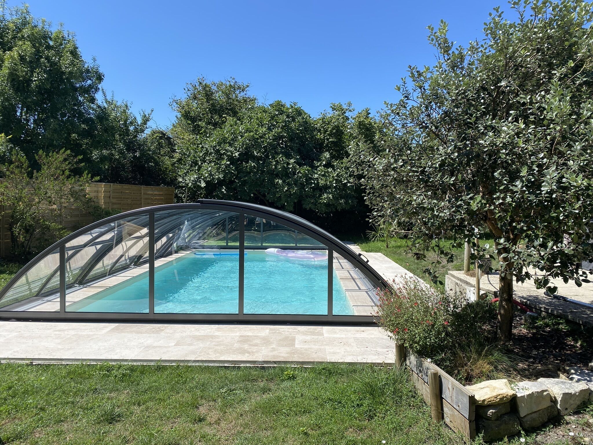 A swimming pool with a glass enclosure, surrounded by a stone deck and greenery.