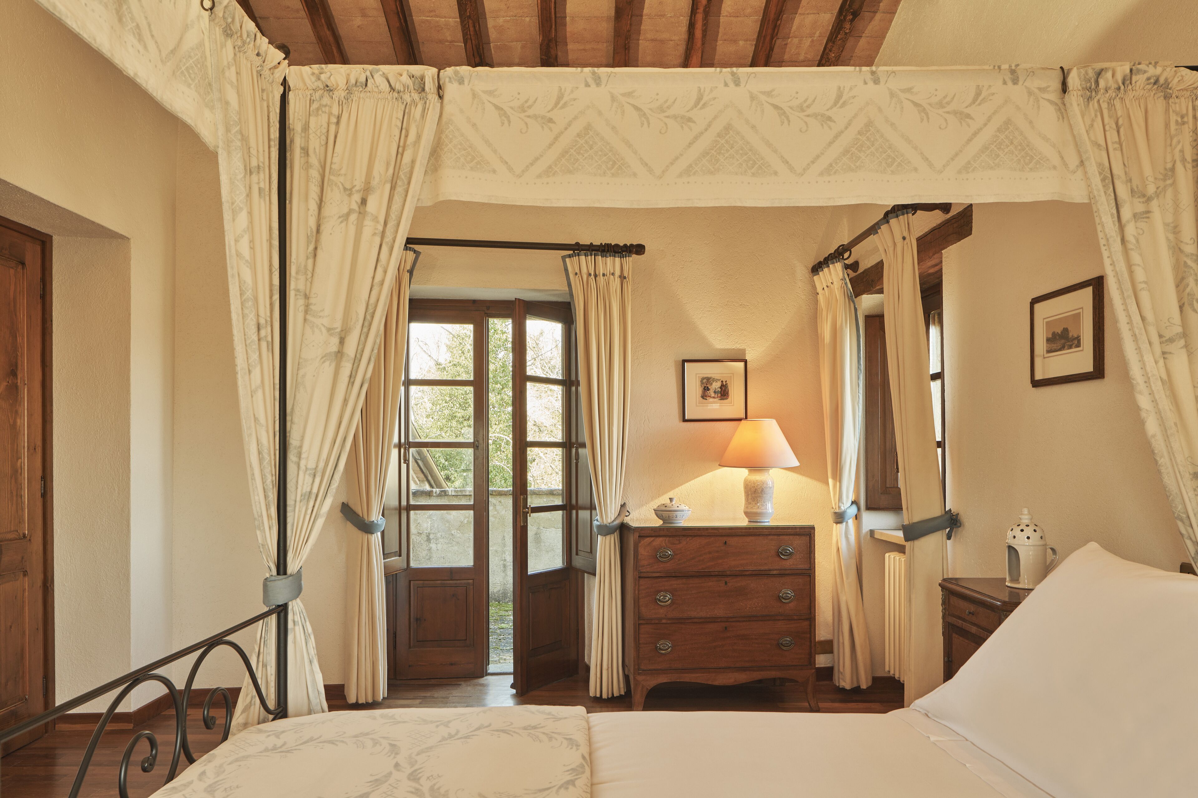 Een slaapkamer met hemelbed, een houten dressoir en een lamp.