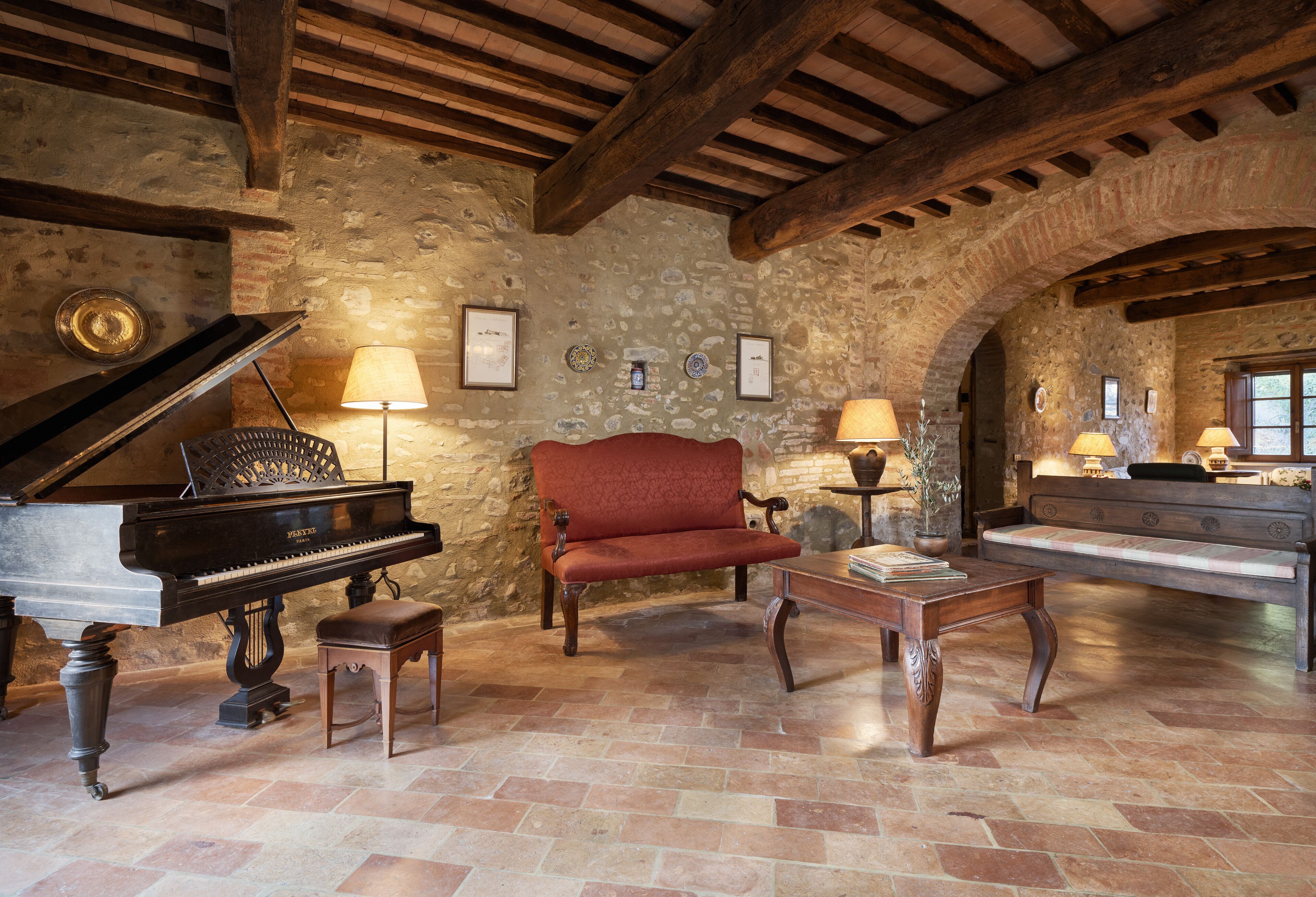 A rustic room with a grand piano, a red sofa, a wooden coffee table, and stone walls.
