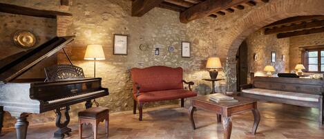 A rustic room with a grand piano, a red sofa, a wooden coffee table, and stone walls.