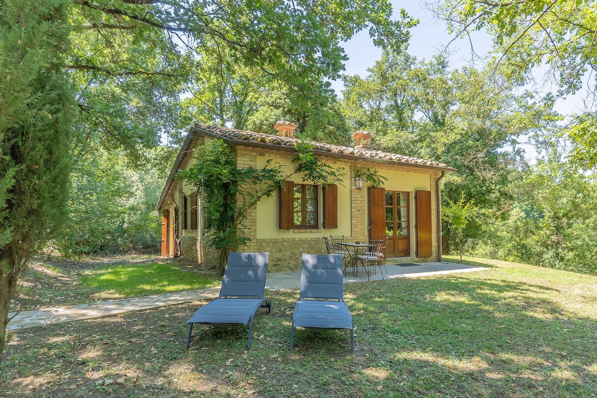A rustic house with a stone facade, a tiled roof, and a small patio with two lounge chairs.