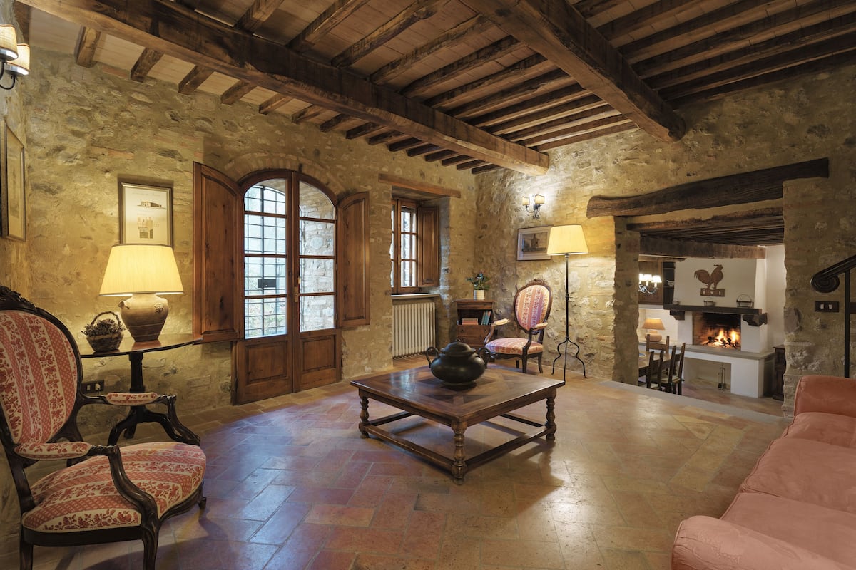 A rustic interior with stone walls, wooden beams, a fireplace, and traditional furnishings.