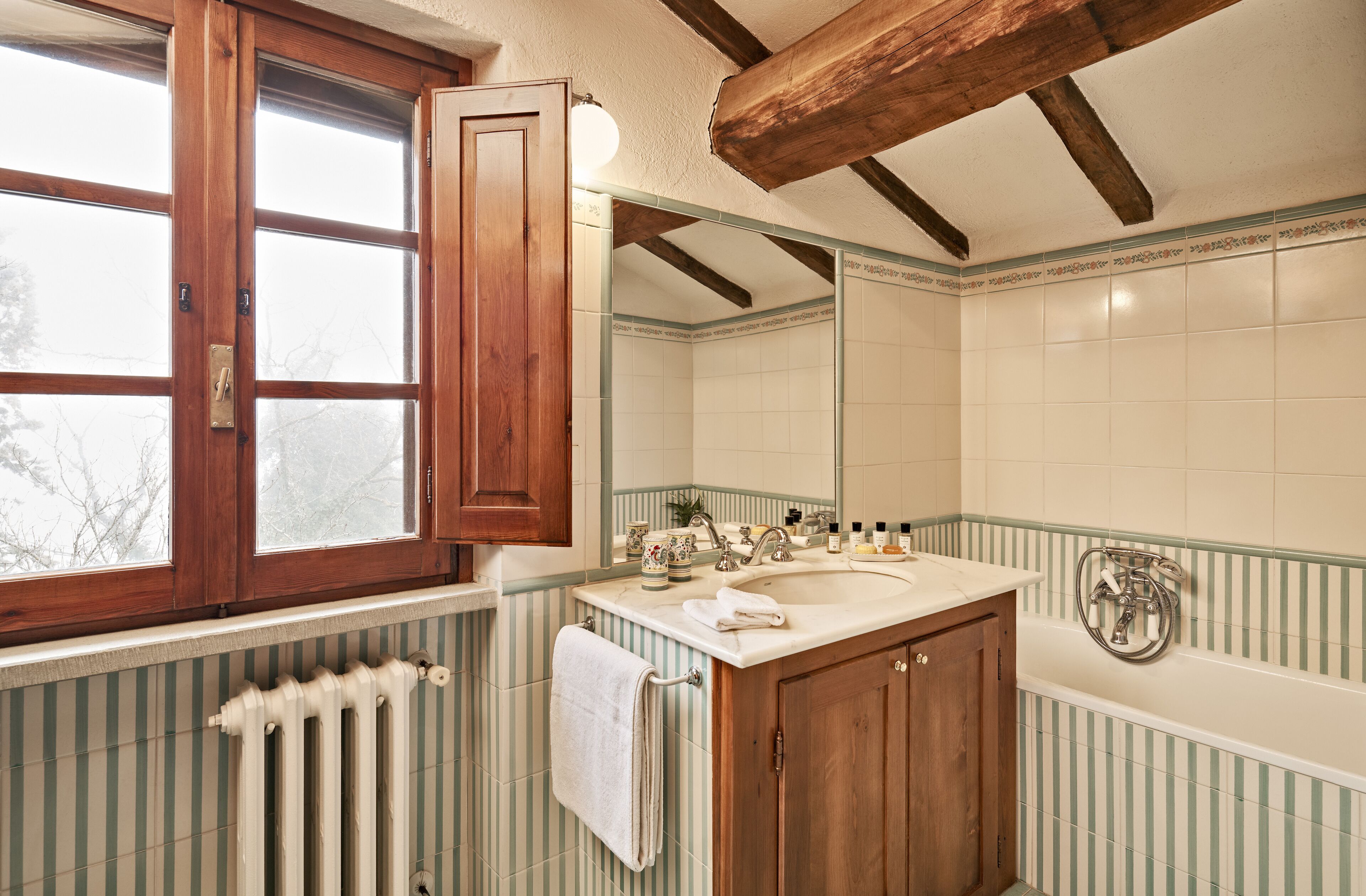 A bathroom with a wooden vanity, a large mirror, and a window with a wooden frame.