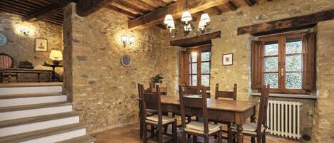 Un comedor rústico con una mesa y sillas de madera, paredes de piedra y una escalera.