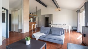 Un salon moderne avec un canapé gris, un plancher en bois, un coin repas avec des meubles blancs et une cuisine dotée de meubles en bois.
