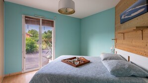 Une chambre à coucher avec un lit, une tête de lit en bois, un luminaire au plafond et une vue sur l’extérieur, accessible par une porte-fenêtre coulissante.