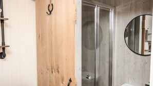 A bathroom with a wooden door, a glass shower enclosure, and a white sink. - Hillside Hut (Ashbourne)