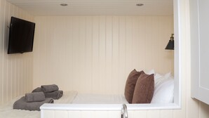 A bedroom with a bed, a TV mounted on the wall, and a bedside lamp. - Hillside Hut (Ashbourne)