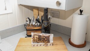 A kitchen counter with a wooden cutting board, a bottle of SORSO, a roll of paper towels, and a utensil holder. - Hillside Hut (Ashbourne)