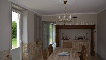 A dining area with a wooden table, wicker chairs, a chandelier, and a stone wall.