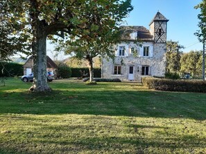Uma casa de pedra com uma torre, cercada por um gramado bem cuidado e árvores.
