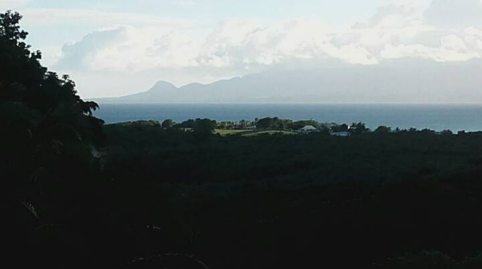 A coastal landscape with a mountain in the distance, a clear sky, and a view of the sea.
