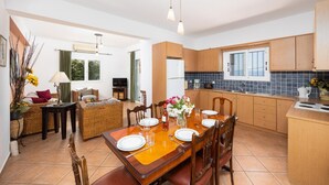 A modern kitchen with wooden cabinets, a dining area with a wooden table and chairs, and a living room with a sofa and a TV.