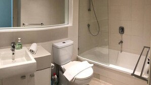 Un baño moderno con ducha envuelta en vidrio, un lavabo blanco con dispensador de jabón y un inodoro.