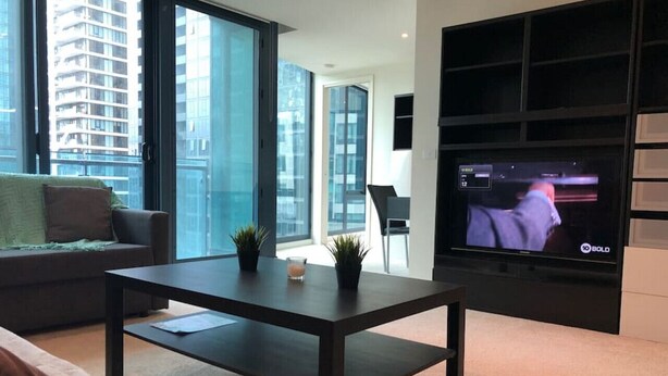 Una sala de estar moderna con un televisor grande, una mesa de centro oscura y un sofá.