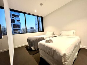 Habitación de hotel moderna con dos camas, un ventanal grande con vistas a la ciudad y una pequeña zona de estar.
