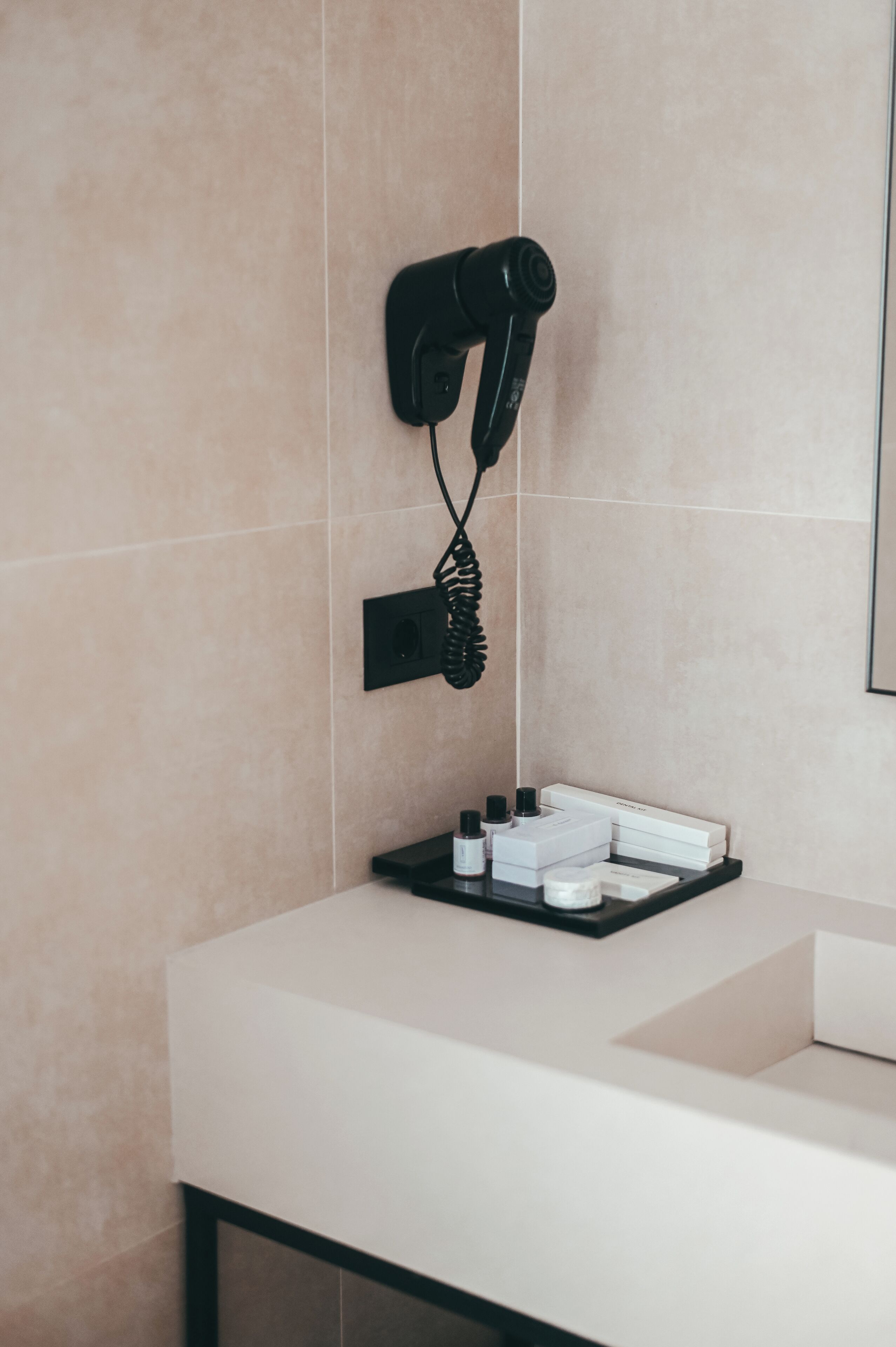 A bathroom with a hairdryer mounted on the wall, a sink, and toiletries on a tray.