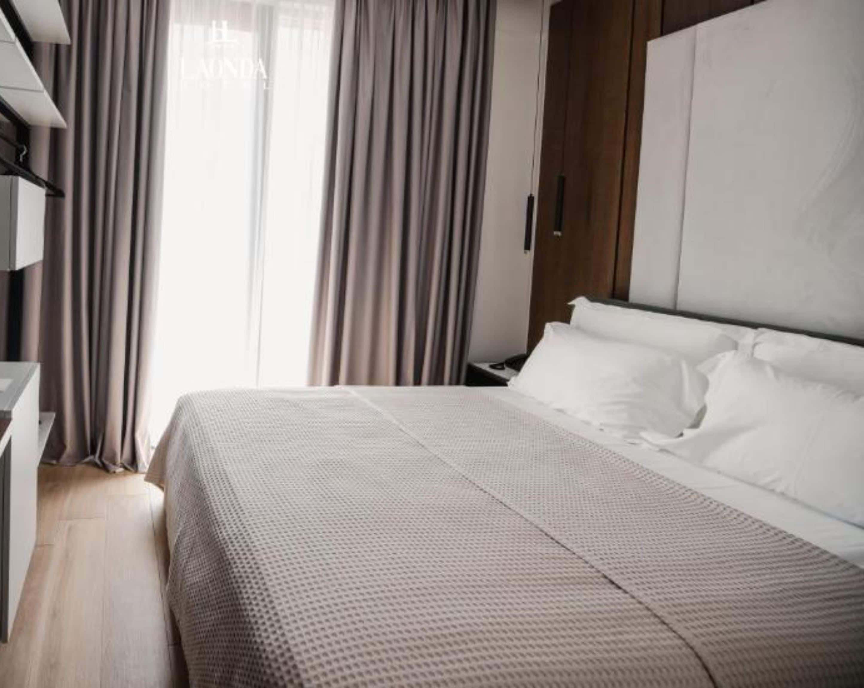 Quarto de hotel com uma cama grande, um guarda-roupa de madeira e uma escrivaninha com cadeira.