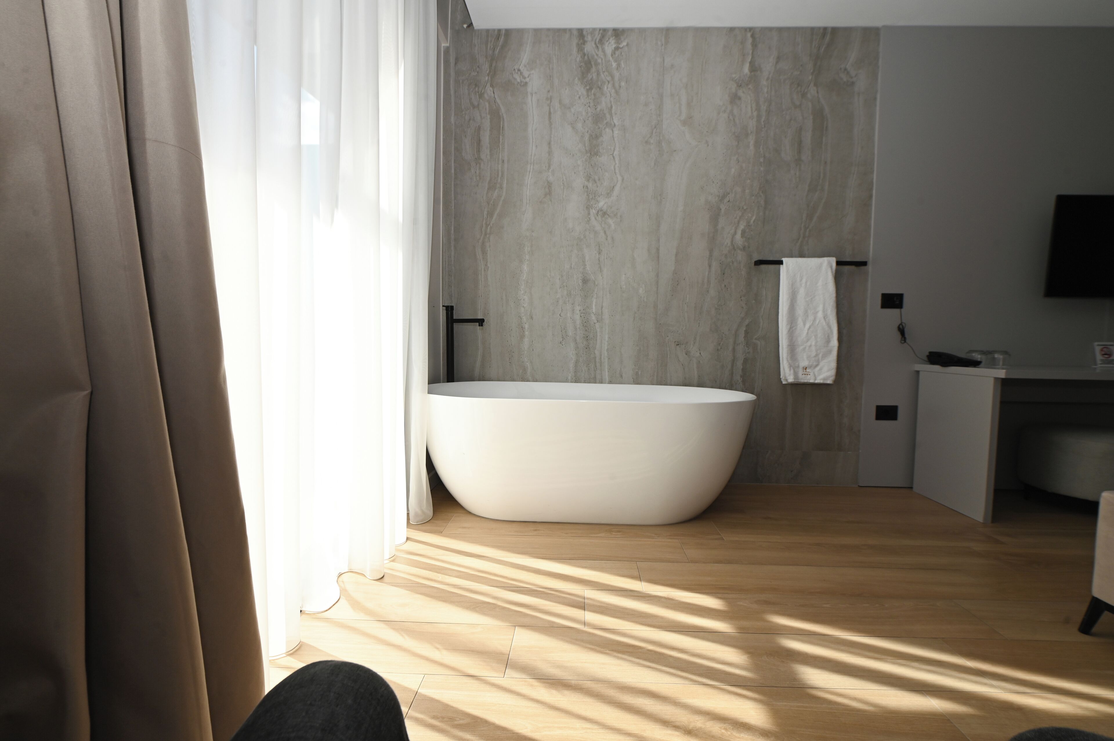 A modern bathroom with a freestanding bathtub, a towel rack, and a flat-screen TV mounted on the wall.