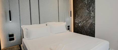 A modern hotel room with a large bed, grey panel headboard, and a marble accent wall.
